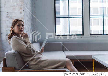 一位女子手捧平板電腦，陷入沉思。 137771359