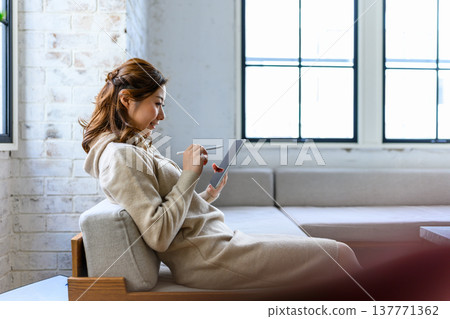 一位女士坐在沙發上，用平板電腦畫畫。 137771362
