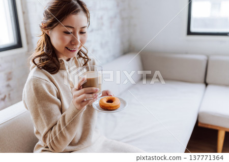 一位女士正在享用甜甜圈和拿鐵咖啡。 137771364