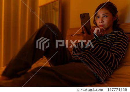 一名婦女在床上的看一個智能手機 137771366