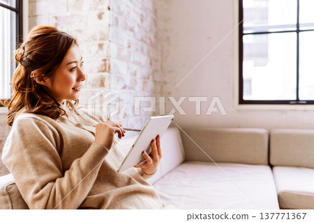 一位女士在室內操作平板電腦時的側臉。 137771367