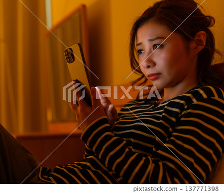 一個女人躺在床上，看著她的智慧型手機，陷入沉思。 137771398