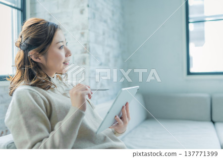 一位女士側臉看著窗邊的平板電腦。 137771399