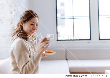 一位女士在家中享用拿鐵咖啡和甜甜圈。 137771401