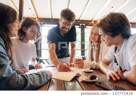 Guy in glasses is standing and explaining project plan. Group of young friends are in the cafe restaurant Guy in glasses is standing and explaining project plan. Group of young friends are in the cafe restaurant 137771419