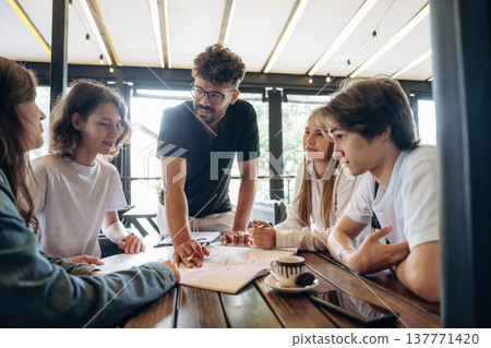 Guy in glasses is standing and explaining project plan. Group of young friends are in the cafe restaurant Guy in glasses is standing and explaining project plan. Group of young friends are in the cafe restaurant 137771420