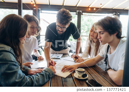 Guy in glasses is standing and explaining project plan. Group of young friends are in the cafe restaurant Guy in glasses is standing and explaining project plan. Group of young friends are in the cafe restaurant 137771421