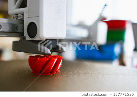 A close-up view of a 3D printer nozzle depositing molten red plastic to build a complex object layer by layer A close-up view of a 3D printer nozzle depositing molten red plastic to build a complex object layer by layer 137771550