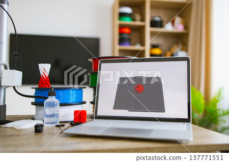 A laptop displays a 3D model next to spools of filament, a 3D printer, and accessories, ready for creation A laptop displays a 3D model next to spools of filament, a 3D printer, and accessories, ready for creation 137771551