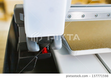 Close-up view of a 3D printer's nozzle depositing molten red filament onto a build plate, showcasing the additive manufacturing process Close-up view of a 3D printer's nozzle depositing molten red filament onto a build plate, showcasing the additive manufacturing process 137771598