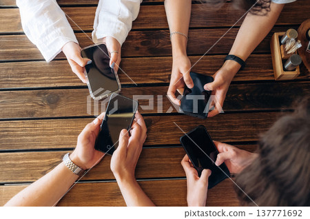 Holding phones. Close up view of young people sitting by the table indoors Holding phones. Close up view of young people sitting by the table indoors 137771692