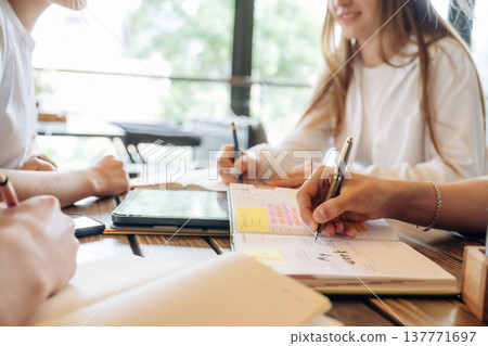 Planning the project, working. Close up view of young people sitting by the table indoors Planning the project, working. Close up view of young people sitting by the table indoors 137771697