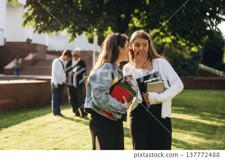 Telling a secret, gossip. Group of students are near university together Telling a secret, gossip. Group of students are near university together 137772488