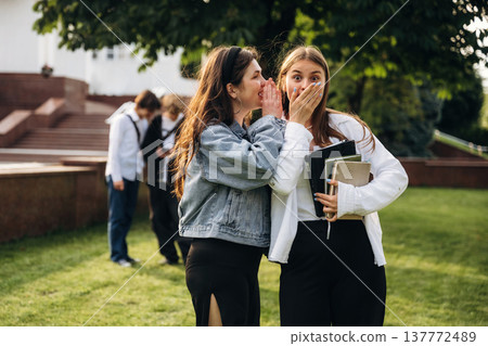 Telling a secret, gossip. Group of students are near university together Telling a secret, gossip. Group of students are near university together 137772489