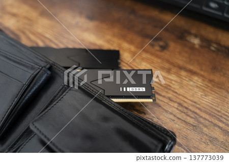 Black DDR5 RAM memory modules placed inside a black wallet on wooden surface. RAM shortages on the market, rising prices, and increased demand driven by the growing need for AI training. Black DDR5 RAM memory modules placed inside a black wallet on wooden surface. RAM shortages on the market, rising prices, and increased demand driven by the growing need for AI training. 137773039