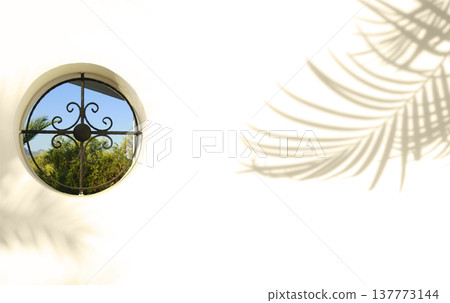 Round window on the white wall backgroung. Shadow of palm trees on the wall. Round window on the white wall backgroung. Shadow of palm trees on the wall. 137773144
