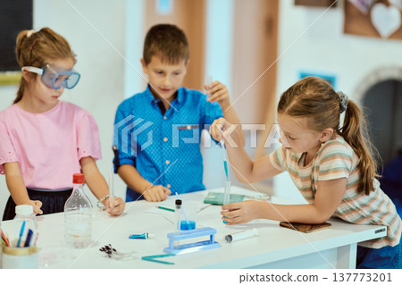 Children doing a hands-on science experiment in a bright classroom learning together 137773201