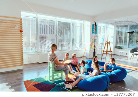Teacher reading to a group of children on beanbags in a bright modern classroom during storytime Teacher reading to a group of children on beanbags in a bright modern classroom during storytime 137773207