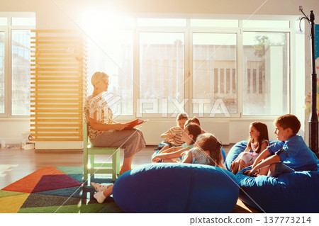 Teacher reading a story to children during storytime in a bright sunny classroom Teacher reading a story to children during storytime in a bright sunny classroom 137773214