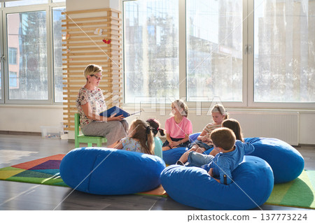 Teacher reading a picture book to young children during cozy classroom circle time on bean bags 137773224