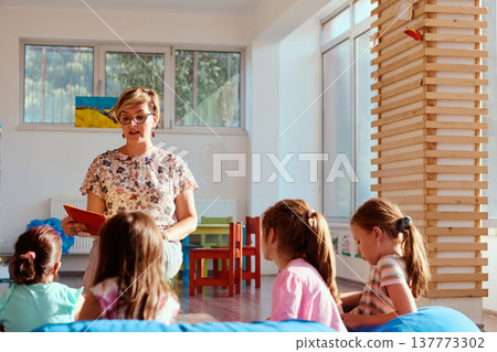Preschool teacher reading a story to attentive children during circle time in a bright classroom 137773302