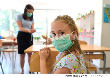 Young student wearing a face mask in a classroom with teacher enforcing safety during pandemic Young student wearing a face mask in a classroom with teacher enforcing safety during pandemic 137773306