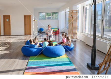 Teacher reading aloud to children sitting on blue beanbags during a bright classroom story time session 137773315