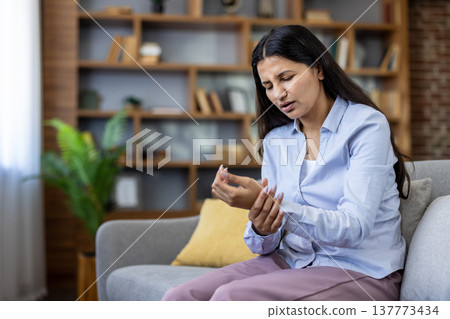 Young woman on a sofa massaging her wrist and hand in pain, showing discomfort from arthritis, carpal tunnel or injury while at home, tired and frustrated Young woman on a sofa massaging her wrist and hand in pain, showing discomfort from arthritis, carpal tunnel or injury while at home, tired and frustrated 137773434