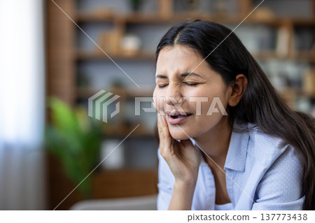 Woman grimacing from a sharp toothache, clutching her cheek and jaw in pain, conveying urgent dental discomfort, worry, and need for immediate dental care or treatment 137773438