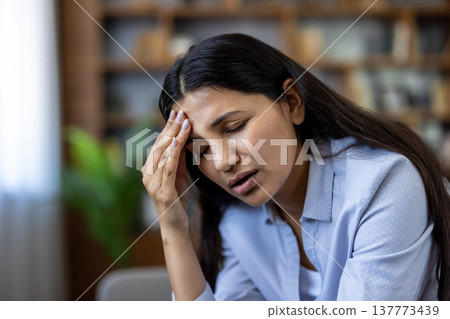 Young woman feeling intense headache and pain, touching her forehead with closed eyes, symbolizing distress, fatigue, and mental exhaustion from overwhelming pressure and daily struggles 137773439