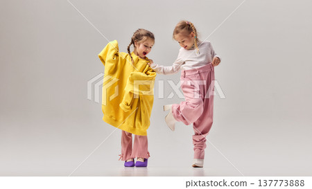 Two little girls laughing and playing together while wearing oversized colorful clothes and high heels in studio. Two little girls laughing and playing together while wearing oversized colorful clothes and high heels in studio. 137773888