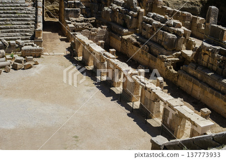 A high-angle horizontal shot showing a row of partially preserved stone pillars (colonnade) and weathered masonry walls within an ancient archaeological site, likely a theater or public building. 137773933