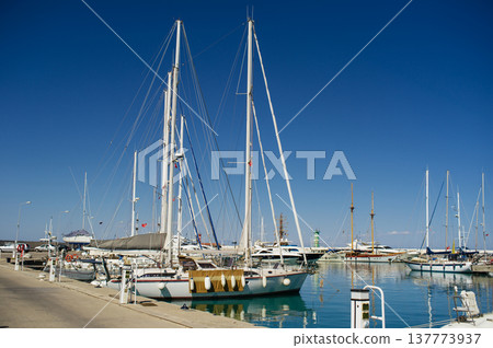A horizontal shot of white luxury yachts and motorboats docked at a pier in a turquoise sea bay under a clear blue sky. 137773937