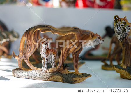 A close-up horizontal shot of detailed animal figurines, including a cheetah standing within an arched wooden branch and a tiger's head, all handcrafted with realistic textures and patterns. A close-up horizontal shot of detailed animal figurines, including a cheetah standing within an arched wooden branch and a tiger's head, all handcrafted with realistic textures and patterns. 137773975