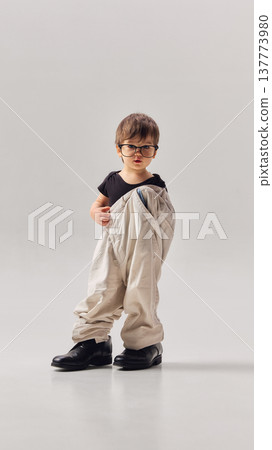 Little boy wearing oversized trousers and glasses posing in studio Little boy wearing oversized trousers and glasses posing in studio 137773980