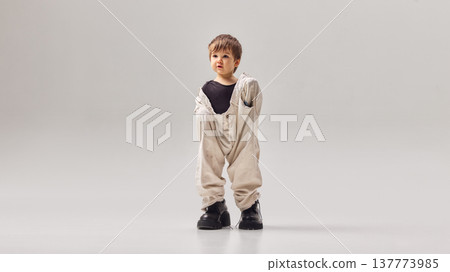 Little boy holding oversized adult trousers and wearing large shoes while standing in studio Little boy holding oversized adult trousers and wearing large shoes while standing in studio 137773985