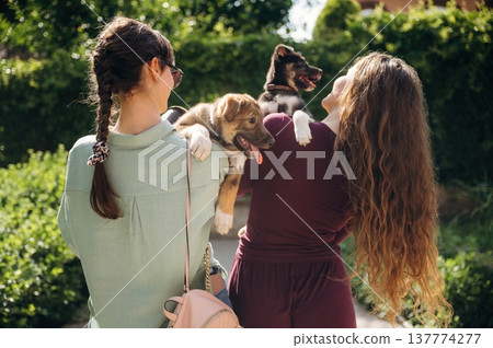 Rear view of two women that are standing and holding dogs in hands Rear view of two women that are standing and holding dogs in hands 137774277