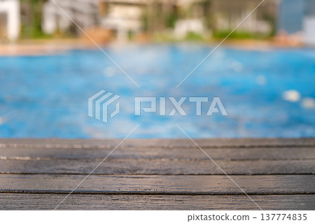 Wooden deck edge overlooking a swimming pool with blue water background 137774835
