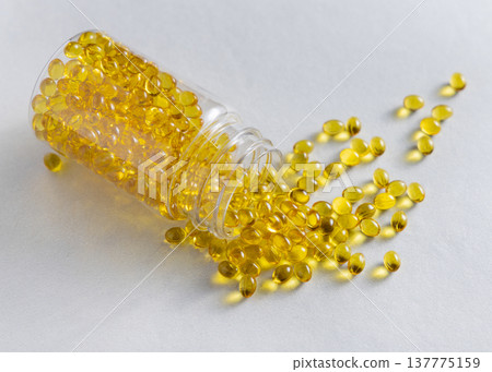 Yellow softgel capsules poured out from transparent bottle on beige stone, healthcare and nutrition 137775159