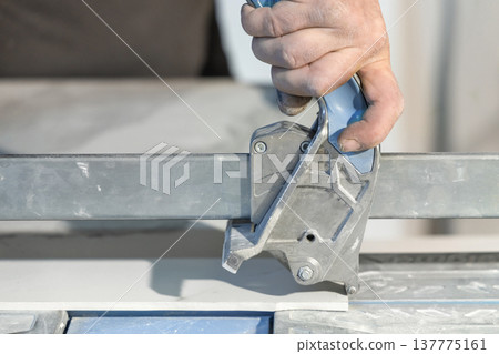 Construction worker hand cutting ceramic tile with manual tile cutter, hand closeup 137775161