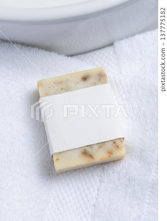 Cream soap bar with blank label on white bath towels near basin, natural hygiene product mockup 137775182