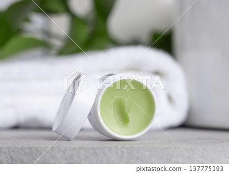 Opened balm jar with natural herbal salve near green leaves in white bathroom, skincare product Opened balm jar with natural herbal salve near green leaves in white bathroom, skincare product 137775193