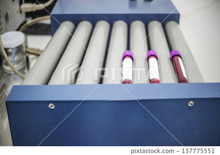 Medical test tubes with blood samples and purple caps rotating on a blue laboratory roller mixer for hematology analysis and diagnostic testing in a clinic 137775551