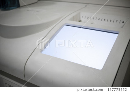 Close-up of a modern laboratory analyzer featuring a glowing touchscreen and numbered slots for medical sample testing, illustrating high-tech diagnostic equipment in a clinical setting Close-up of a modern laboratory analyzer featuring a glowing touchscreen and numbered slots for medical sample testing, illustrating high-tech diagnostic equipment in a clinical setting 137775552