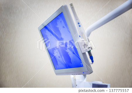 Close-up of a professional dental monitor on an articulated arm, showing diagnostic images in a blue tone with an intraoral camera tool attached in a clinical office setting Close-up of a professional dental monitor on an articulated arm, showing diagnostic images in a blue tone with an intraoral camera tool attached in a clinical office setting 137775557