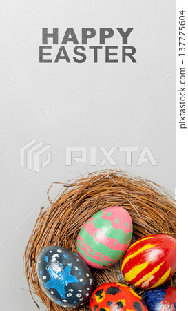 A vertical greeting card for Easter featuring hand-painted colorful eggs resting in a rustic nest made of twigs, set against a clean gray background with the text 'HAPPY EASTER' A vertical greeting card for Easter featuring hand-painted colorful eggs resting in a rustic nest made of twigs, set against a clean gray background with the text 'HAPPY EASTER' 137775604