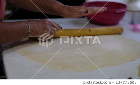 Hands roll out a thin sheet of dough using a wooden rolling pin on a kitchen work surface. The footage shows traditional home baking preparation, useful for cooking tutorials, homemade food visuals Hands roll out a thin sheet of dough using a wooden rolling pin on a kitchen work surface. The footage shows traditional home baking preparation, useful for cooking tutorials, homemade food visuals 137775605