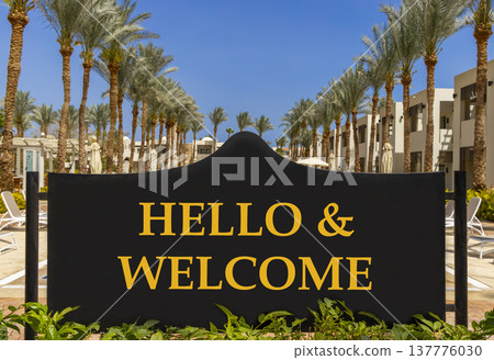 Hello and welcome symbol. Concept words Hello and welcome on beautiful big black road sign. Beautiful blue sky palm trees background. Business hello and welcome concept. Copy space. Hello and welcome symbol. Concept words Hello and welcome on beautiful big black road sign. Beautiful blue sky palm trees background. Business hello and welcome concept. Copy space. 137776030