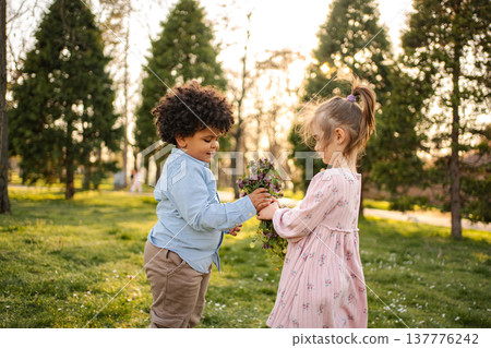Boy giving flowers to girl, children playing in park Boy giving flowers to girl, children playing in park 137776242