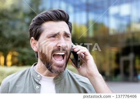 Frustrated man expressing anger and screaming into smartphone during difficult conversation or conflict, displaying strong negative emotions and despair 137776406